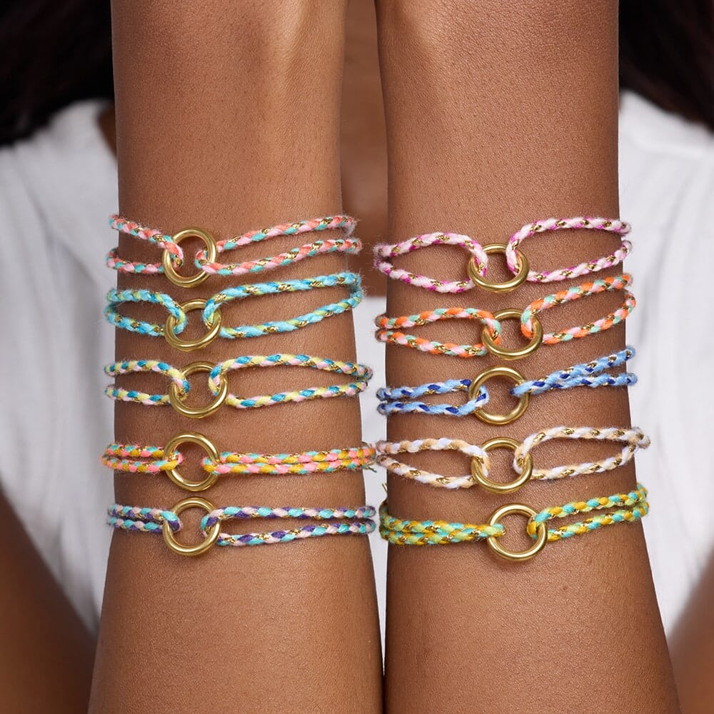 Multicolored braided bracelets with gold loops on a person's wrist against a white background