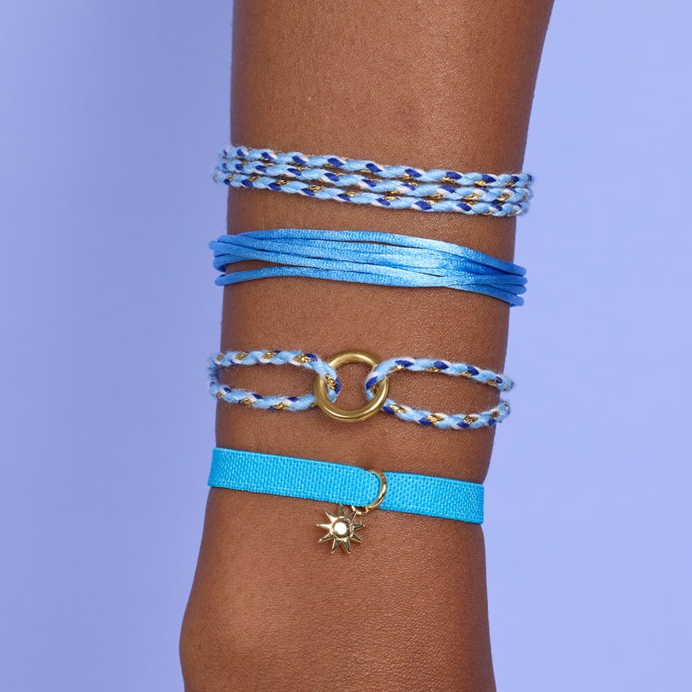 Wrist with multiple blue bracelets on a purple background
