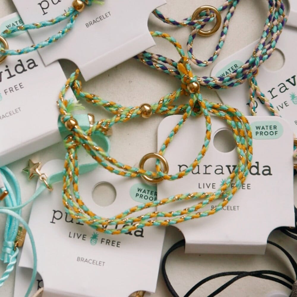 Multiple braided bracelets with gold accents on Puravida branded cards.