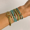 Wrist with multiple turquoise and gold bracelets on a neutral background