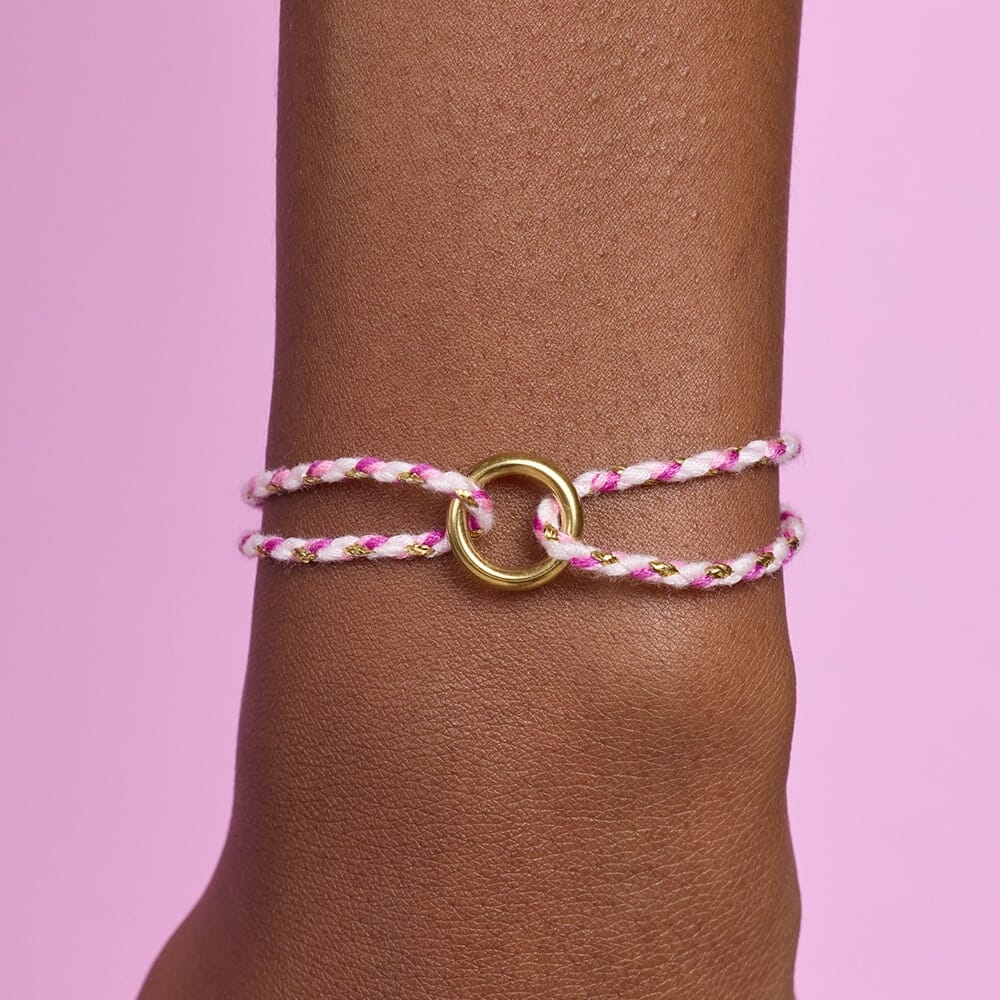 Bracelet with pink and gold design on a wrist against a pink background