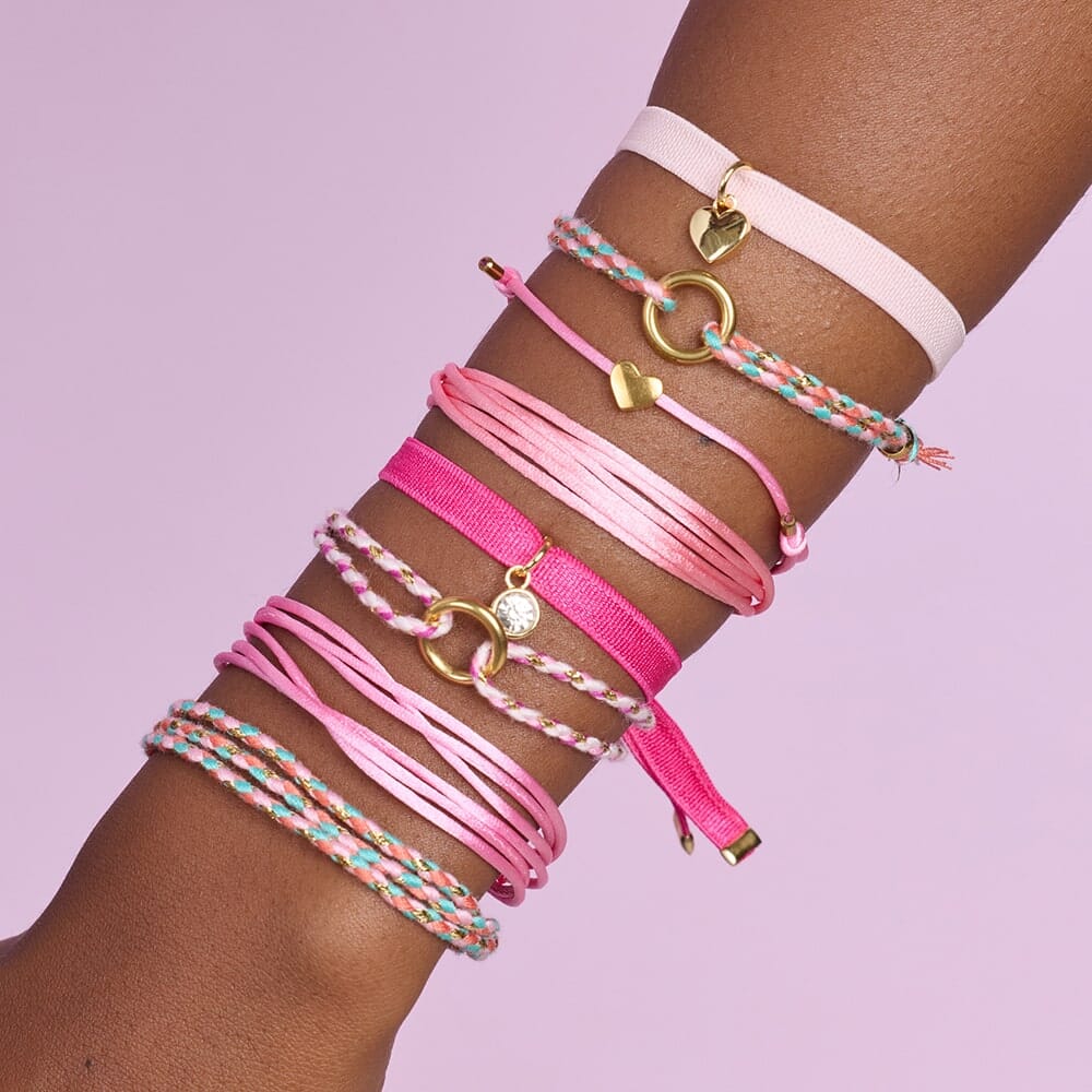 Multicolored bracelets on a wrist against a pink background