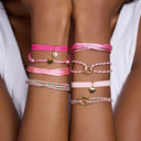 Close-up of a person's wrist wearing multiple pink bracelets with heart and circle charms.
