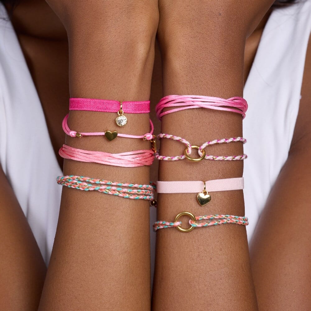Close-up of a person's wrist wearing multiple pink bracelets with heart and circle charms.