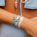 Close-up of a wrist wearing multiple colorful bracelets on a neutral background