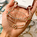 Hand holding a colorful braided bracelet with a gold clasp on a blurred background