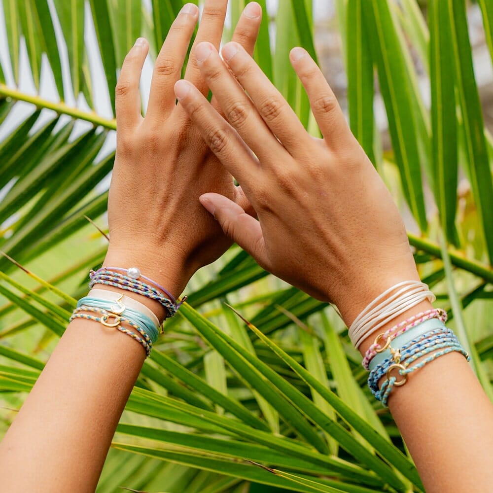 Two hands with multiple bracelets on a background of green leaves