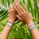 Two hands with multiple bracelets on a background of green leaves