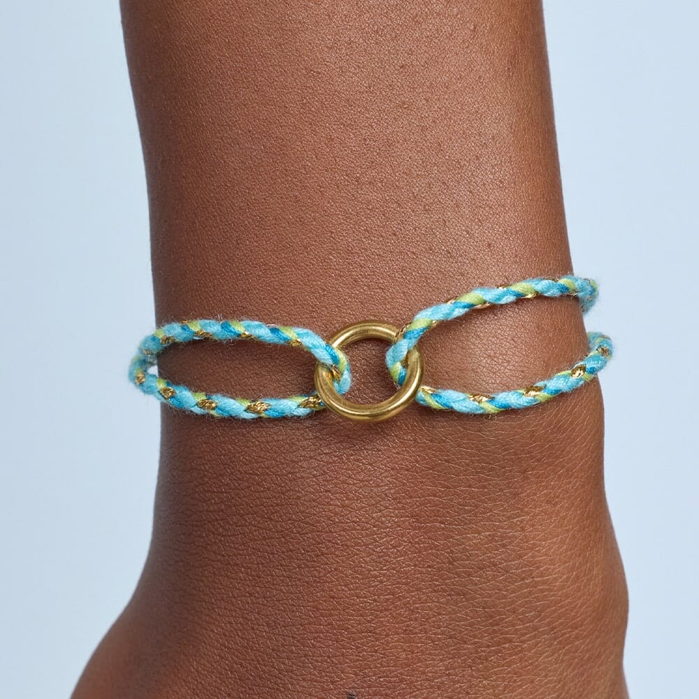 Bracelet with blue and gold design on a wrist against a light blue background