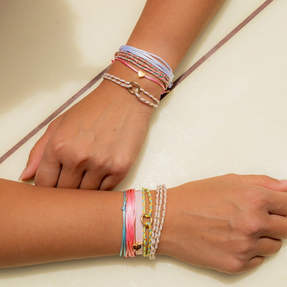 Two wrists wearing multiple colorful bracelets on a light background