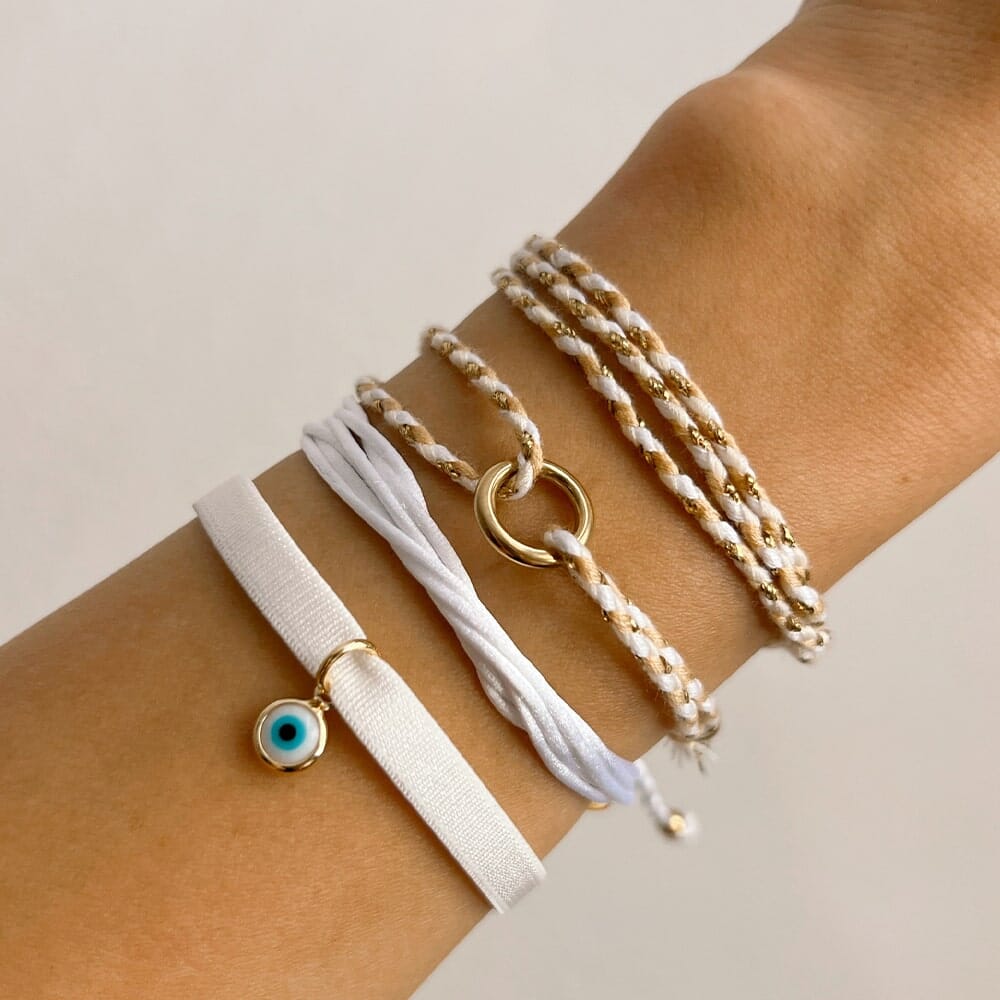 Wrist with multiple bracelets including a white one with an eye charm on a neutral background